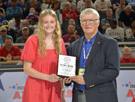 Kaitlin White of Columbus North (left) receives a plaque from Steve Witty in recognition of her winning one of the inaugural Steve & Jeanie Witty Scholarship awards at the 2024 Indiana-Kentucky All-Star doubleheader in Gainbridge Fieldhouse.
